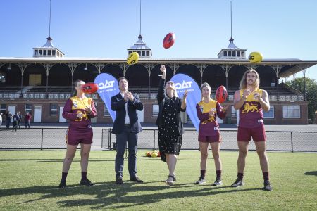 two women and one male football players with AFL Victoria head and TAC representatives handballing footballs into the air.
