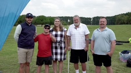 Five people facing the camera next to a banner with TAC branding , standing on a golf course. 