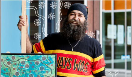 Man holding First Nations Artwork wearing Always Was black, red and gold jumper.