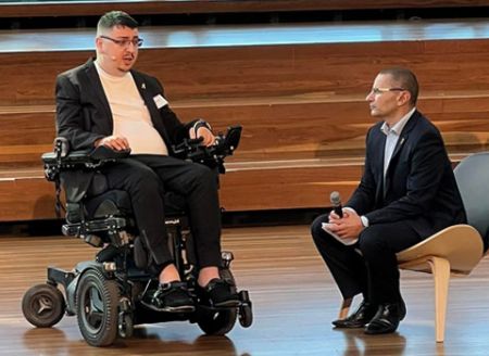 Man in wheelchair with microphone. Man sitting down with microphone. 