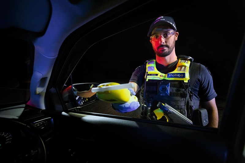 A male police officer holding out a breath test machine