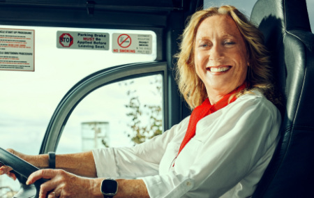 Woman with hands on the steering wheel of a bus smiling.