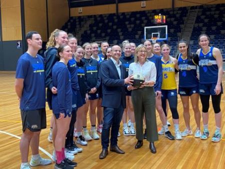 A man and a woman holding a basketball surrounded by women's basketball players.