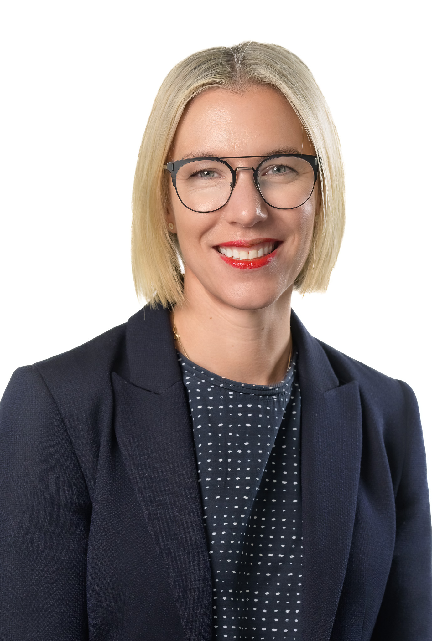Woman smiling to camera wearing glasses, a dark shirt with white flecks and a blazer.