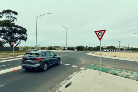 Image of a sedan car stopping at a give way sign before heading into a roundabout.