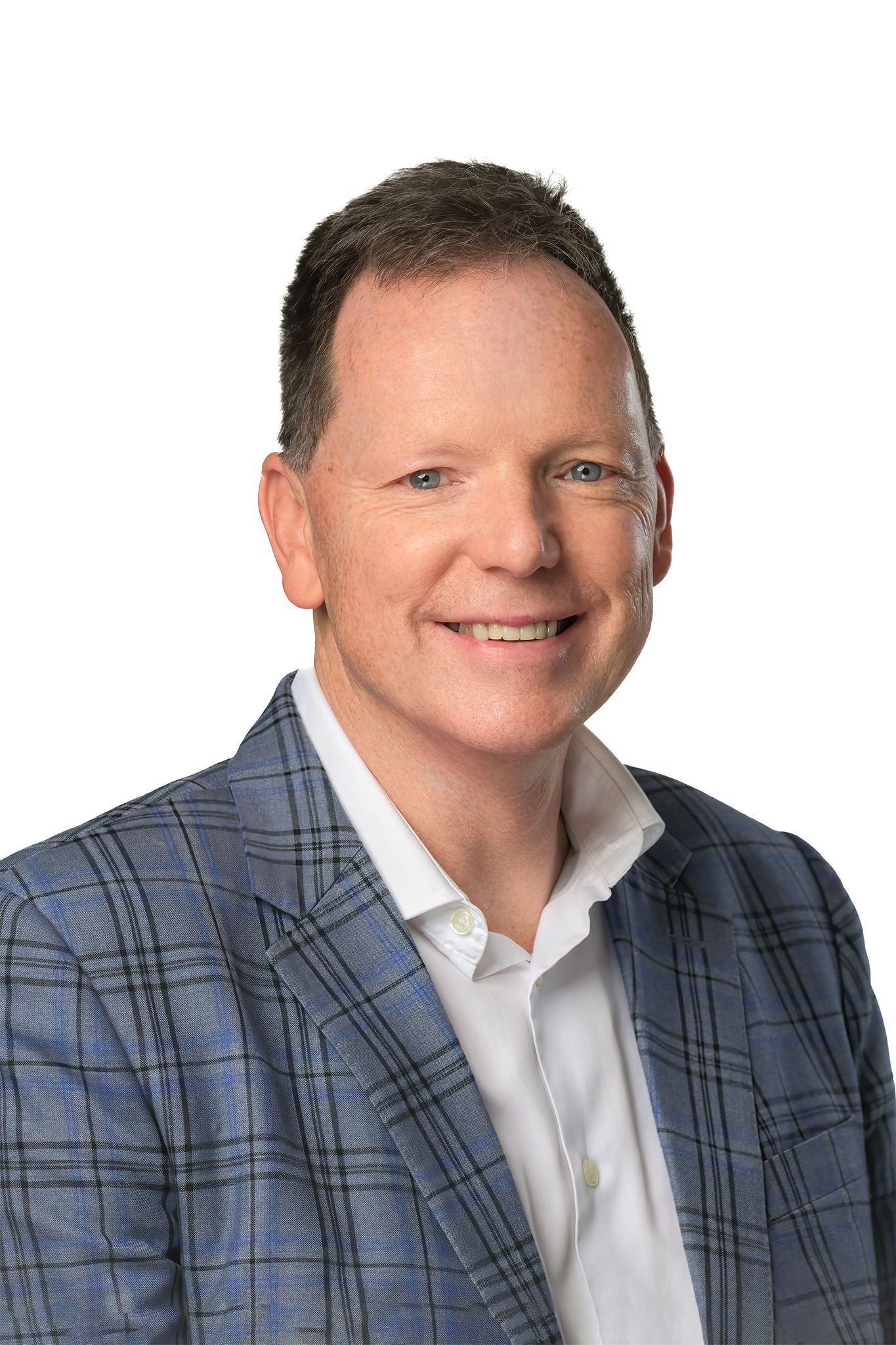 Photo of man smiling to camera against a white background wearing a white open neck shirt and blue checked blazer