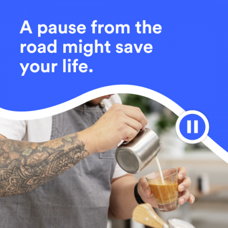 A pause from the road might save your life. A male barista with a tattooed arm is pouring milk from a coffee jug into a glass cup.