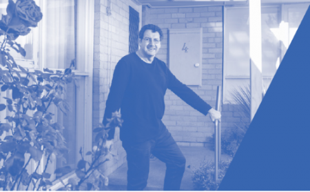 Man dressed in black standing near the front door of a house. 