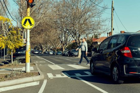 Local street scene with a car stopped at a pedestrian crossing where a man crosses